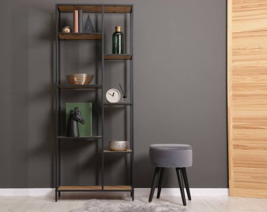 Shelving unit with decor, stool and folding screen near grey wall indoors