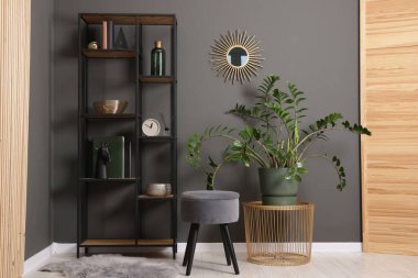 Shelving unit with decor, stool and folding screen near grey wall indoors