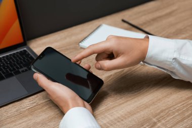 Adam ahşap masada boş ekranlı akıllı telefon kullanıyor.