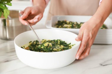 İçerideki mermer masada ıspanaklı lazanya yapan kadın, yakın plan.