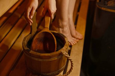 Saunada bir kova suyu olan kadın, yakın plan.