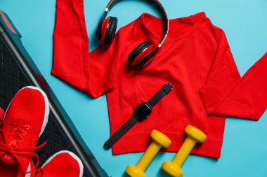 Different gym stuff, wrist watch and headphone on light blue background, flat lay