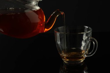 Çaydanlıktan taze demlenmiş çayı siyah masaya, cam fincana dökerek.