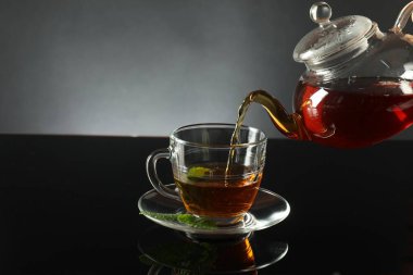 Koyu ayna masasında çaydanlıktan fincana taze demlenmiş çay dökülüyor.