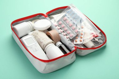 İlk yardım çantası. Turkuaz arka planda çantanın içinde farklı tıbbi malzemeler var.