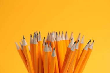 Many graphite pencils on orange background, closeup