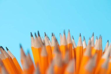 Many graphite pencils on light blue background, closeup