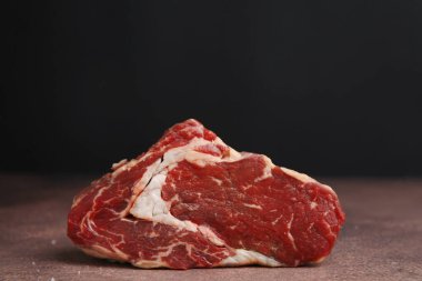One piece of raw beef on brown textured table against black background, closeup