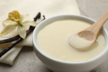 Lezzetli konsantre süt, vanilya kabukları, çiçek ve kaşık açık gri masada, yakın plan.