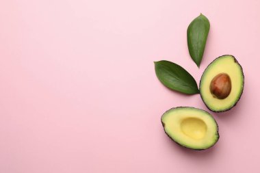 Bir kesik olgun avokado ve pembe arka planda yapraklar, düz. Metin için boşluk