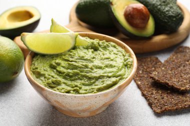 Lezzetli avokado sosu, limon ve gevrekler açık gri masada, yakın plan.