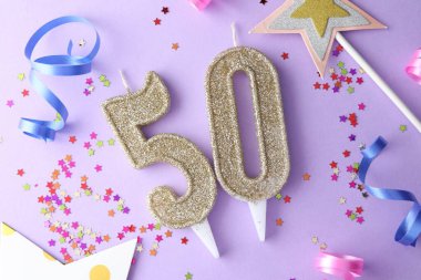 50th birthday. Number shaped candles, confetti and party decor on violet background, flat lay