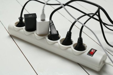 Eklenti güç panosu beyaz ahşap zeminde tıkaçlarla aşırı yüklenmiş, yakın plan.