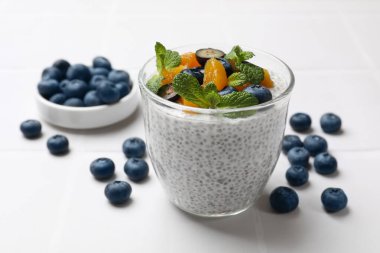 Delicious chia pudding with blueberries, peaches and mint in glass on white table, closeup