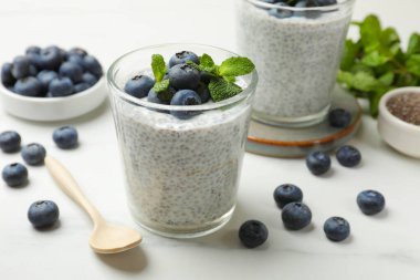 Delicious chia pudding with blueberries and mint in glasses on white table, closeup