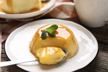 Karamel soslu lezzetli puding ve ahşap masada servis edilen nane, yakın plan.