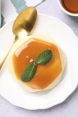 Delicious pudding with caramel sauce and mint served on light table, flat lay