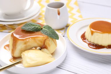 Delicious pudding with caramel sauce and mint served on white wooden table, closeup