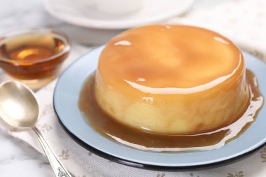 Karamel soslu lezzetli puding ve beyaz masada kaşık, yakın plan.