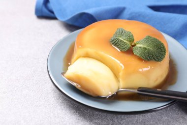 Karamel soslu lezzetli puding, gri desenli masada nane ve kaşık, yakın plan. Metin için boşluk