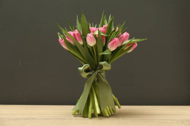 Gri arka planda, ahşap masanın üzerinde duran güzel laleler.