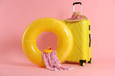 Sarı şişirilebilir yüzük, bavul ve pembe arka planda plaj aksesuarları.