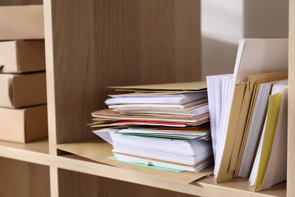 Different paper envelopes and parcels on wooden shelves in post office, closeup