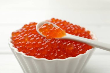 Lezzetli kırmızı havyar kasede ve kaşıkta beyaz masada, yakın plan.