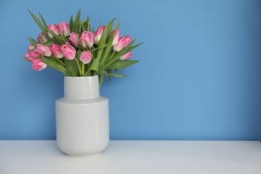 Beyaz masadaki vazodaki güzel lalelerin buketi açık mavi arkaplan, metin için alan