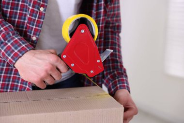 Karton kutuyu kapalı bir yere kapatmak için yapıştırıcılı bant kullanan bir adam.