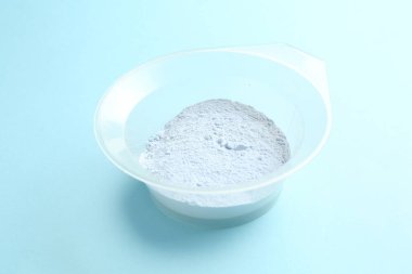 Açık mavi arka planda saç ağartma tozu olan kase, yakın plan.