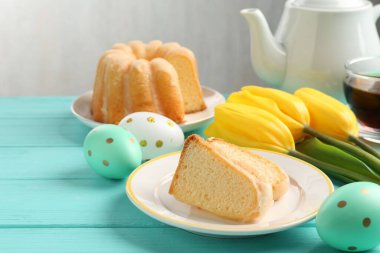 Lezzetli kek parçaları, Paskalya yumurtaları, laleler ve çay açık mavi ahşap masada.