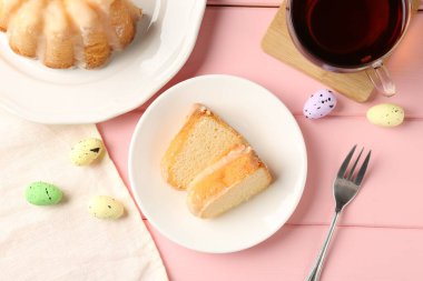 Lezzetli kek parçaları, pembe ahşap masada paskalya yumurtası ve çay, düz uzanma.