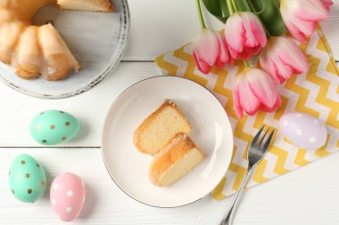 Lezzetli kek parçaları, beyaz ahşap masada paskalya yumurtası ve laleler.