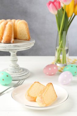 Lezzetli kek parçaları, beyaz ahşap masada paskalya yumurtaları ve laleler.