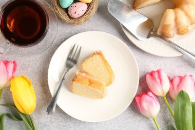 Lezzetli kek parçaları, Paskalya yumurtaları, laleler ve çay gri masada, düz yatıyordu.