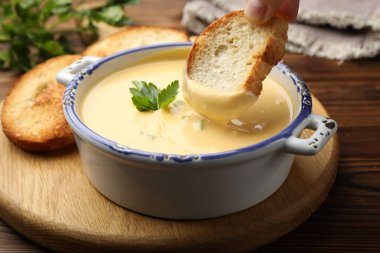 Ahşap masada ekmeği lezzetli peynir sosuna batıran kadın, yakın plan.