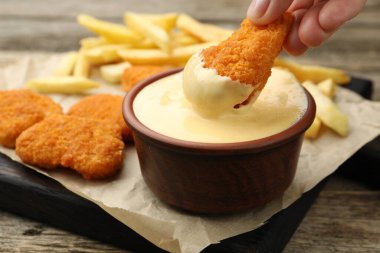 Ahşap masada tavuk parçalarını peynir sosuna batıran kadın, yakın plan.