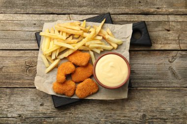 Tabakta leziz peynir sosu, tavuk nugget ve ahşap masada patates kızartması.