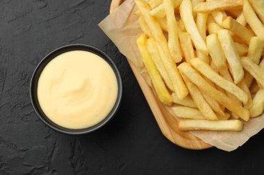 Tabakta leziz peynir sosu ve siyah masada patates kızartması.