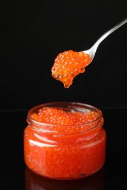 Siyah arka planda kavanozdan kaşıkla kırmızı havyarı almak, yakın plan.
