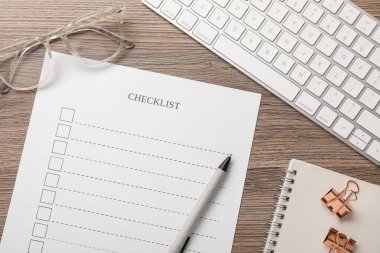 Kontrol listesi, kalem, gözlük, ataç ve klavye tahta masada, düz konum