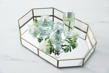 Parfümlü tepsi ve beyaz masada güzel çiçekler.