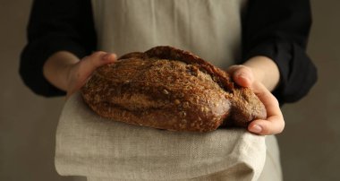 Gri arka planda taze ekmek somunu olan kadın, yakın plan.