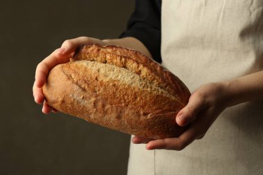 Gri arka planda taze ekmek somunu olan kadın, yakın plan.