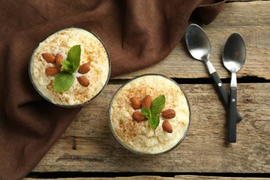 Tarçınlı lezzetli sütlaç, badem ve nane şekeri ahşap masada servis edilir.
