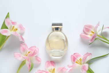 Bir şişe parfüm ve beyaz arka planda güzel çiçekler.