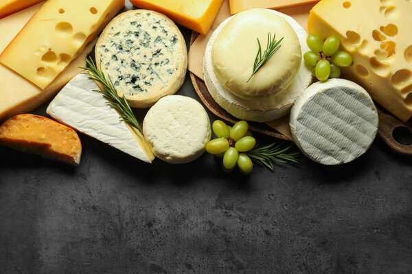 Different types of cheese, rosemary and grapes on dark textured table, flat lay. Space for text