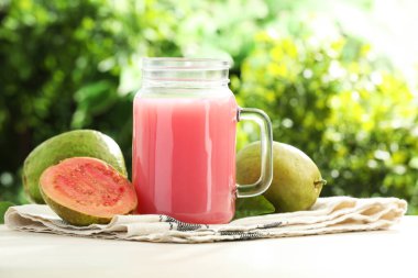 Mason kavanozunda lezzetli guava suyu ve açık havada beyaz masada taze meyve, yakın plan.