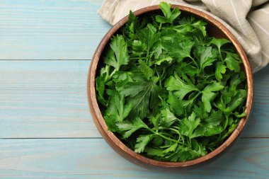 Açık mavi ahşap masada, kasede taze maydanoz yaprakları, üst manzara. Metin için boşluk